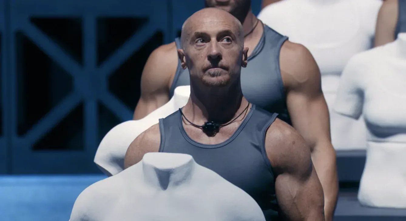 An athlete standing beside a torso sculpture in Physical 100 Italy.