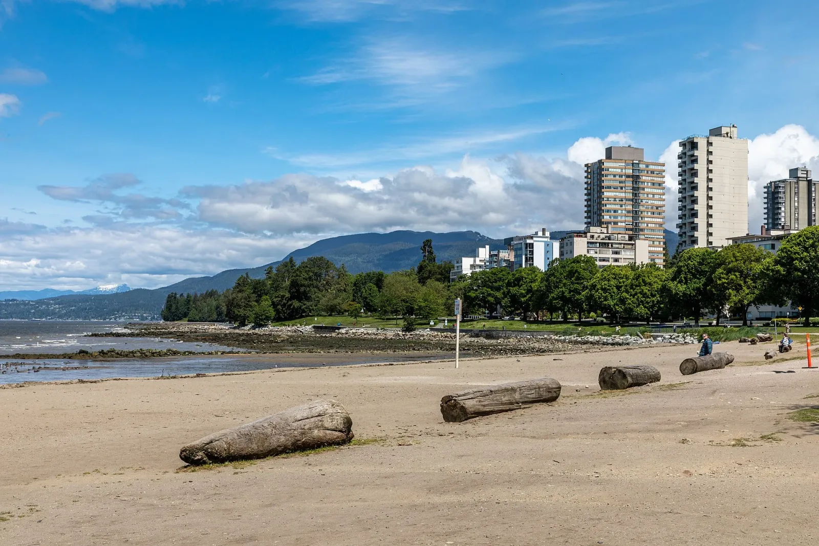 Sand, driftwood logs and waterfront buildings at English Bay Beach.