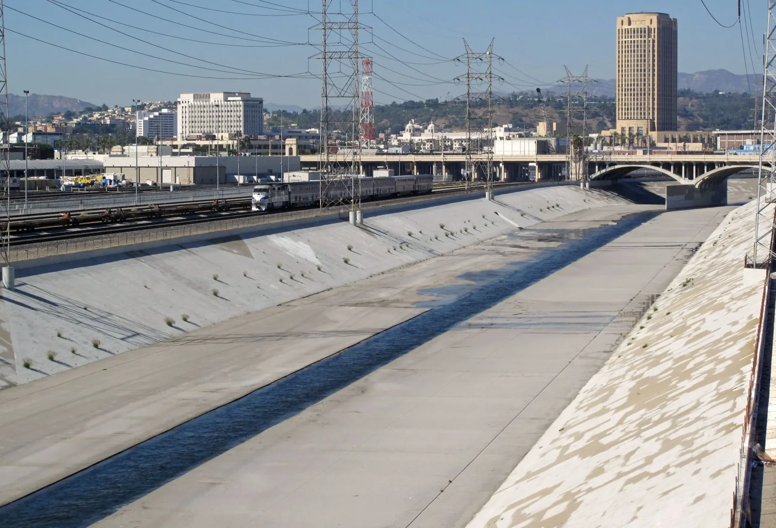 Concrete channel of the Los Angeles River with railway tracks, bridges and city buildings.