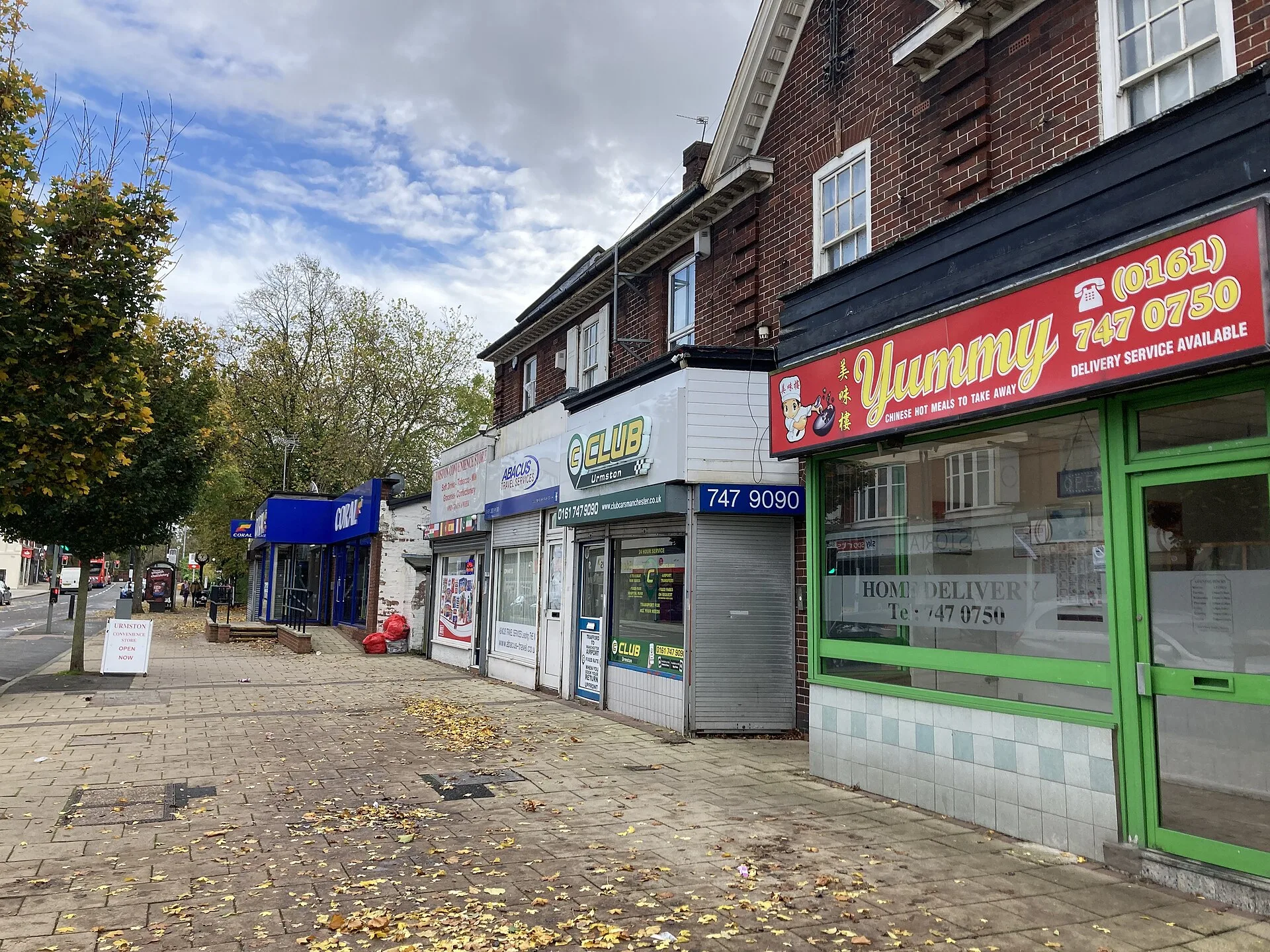 A row of shops beside the sidewalk on Flixton Road in Urmston.